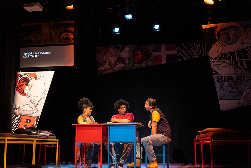 Three kids on a stage sitting around a table