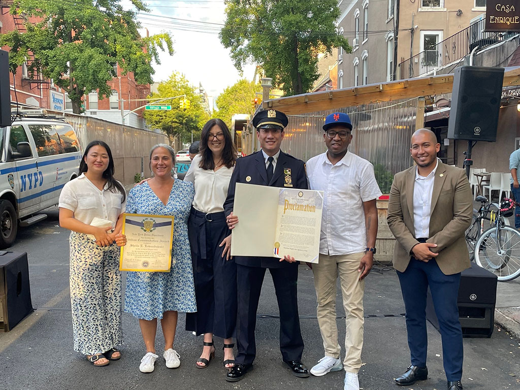 LPC Chair Sarah Carroll stands with Council Member Julie Won, Queens Community Board 2 member, NYPD Captain Tony Wong, Queens Borough President Donovan Richards, and  Assembly Member Juan Ardila; group is displaying mayoral proclamation