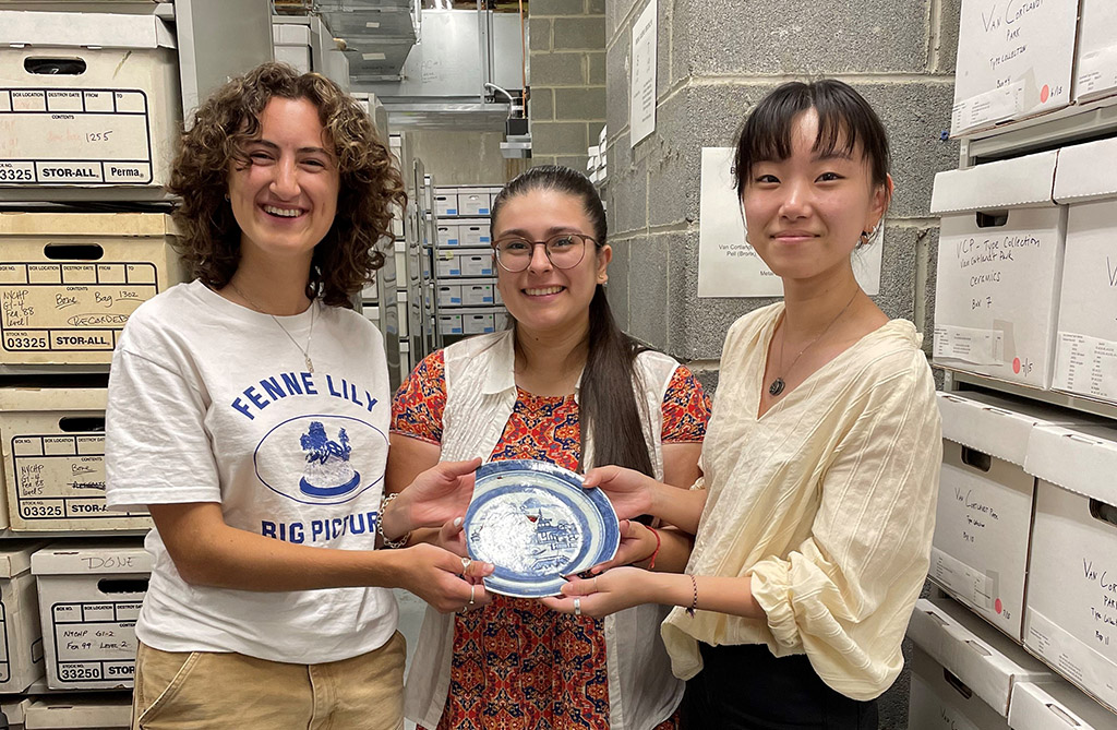 Three female interns holding an carefully holding an artifiact inside an archive document room