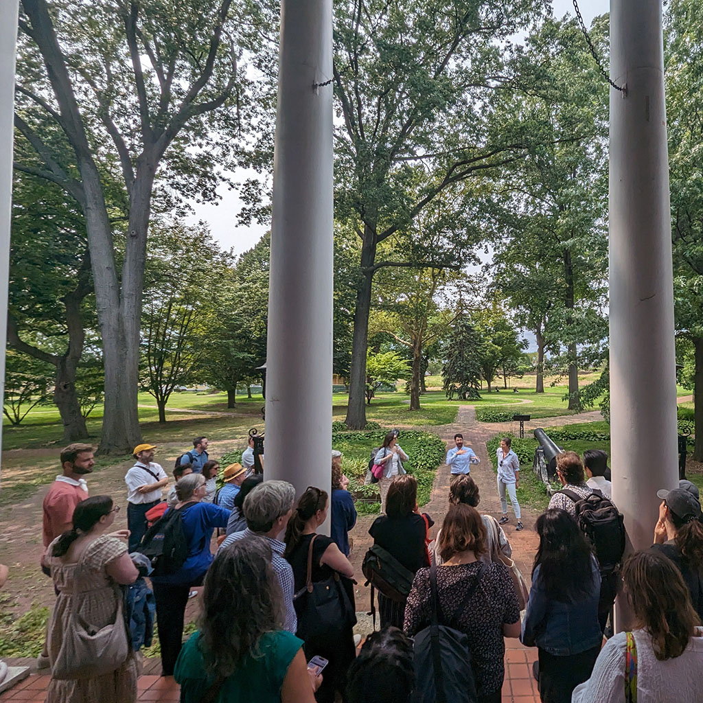 A group of people stands on steps looking out at green lawn