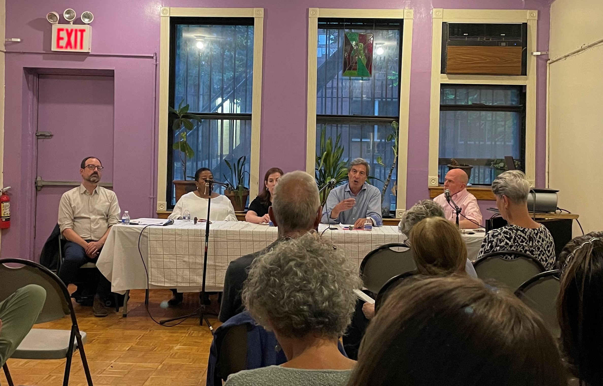 A group of people sitting at a long table at the front of a room speaking to audience members seated in front of them