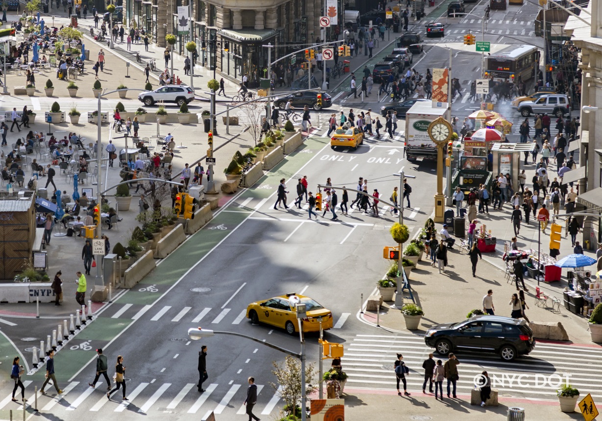 A busy NYC street with pedestrians crossing in crosswalk