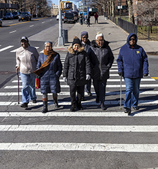 A group of six older adults cross a street on the crosswalk.