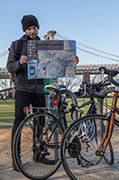 A person standing in park beside a bike rack looks at a paper map.