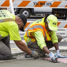 Two NYC D O T employees install a pedestrian ramp on a street corner.