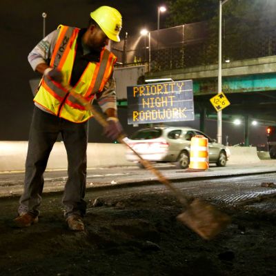 An N Y C D O T employee uses a shovel to mill a roadway.