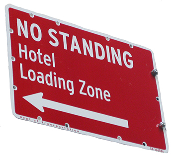Red street sign with white text stating No Standing. Hotel Loading Zone with a white arrow pointing left.