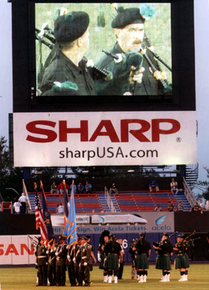D.S.N.Y. Emerald Society Pipe and Drum Band joins with Honor Guard in center field while jumbotron captures action