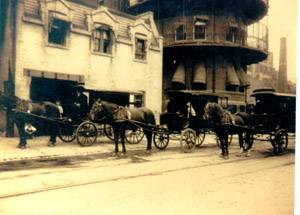 Three horse-drawn ambulances stand outside Gouverneur Hospital, circa 1900
