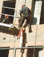 Picture of Firefighters training in rope rescues as they lower themselves down the side of a building via harness and rope to rescue a practice manequin.