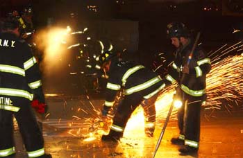 Firefighters, battling a 3-Alarm blaze, vent the roof of a plumbing supply warehouse involved.