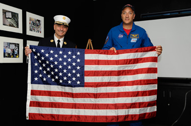 Astronaut Michael J. Massimino and Chief of Department Salvatore Cassano hold the flag flown on the Space Shuttle Atlantis, which will be given to the City of New York in honor of all those who were killed on Sept. 11, 2001.