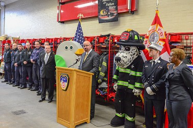 FDNY Deputy Commissioner for Support Services John Benanti (at podium) speaks about FDNY energy efficiency with DCAS Commissioner Edna Wells Handy (far right); Hot Dog, the FDNY fire safety mascot; Birdie, GreeNYC's mascot; and the members of Engine 258/Ladder 115).