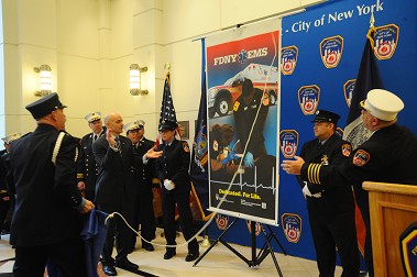 Fire Commissioner Salvatore Cassano and Chief of EMS Abdo Nahmod watch as Paramedic Jessica DeResto and EMT David Weissman unveil the 2014 EMS Week poster in which they are featured.