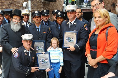 Firefighters from Engine 211, Ladder 119 and Rescue 2, who saved 7-year-old Mendy Gottlieb (center) receive plaques for their firehouses.