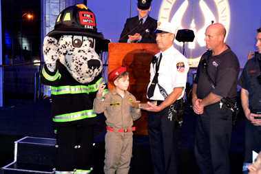 Deputy Chief Anthony Devita and Hot Dog, the FDNYâ€™s Fire Safety Mascot, and the members of Ladder 16 stand by Jao Daniel de Barros, as FF Carlos Azevedo, Engine 316, swears him in as a Junior FDNY Firefighter.