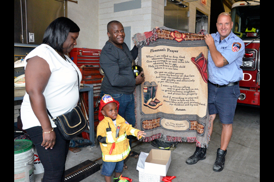 (from left to right) Danae Pierre, Justin Chase Pierre and Jean Pierre present Lieutenant Victor Milukas of Ladder Company 159 a blanket with the Firemanâ€™s Prayer. 