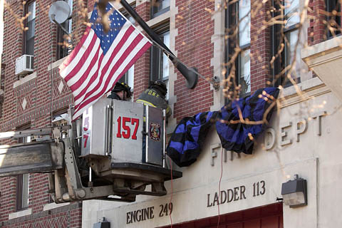 Firefighter Matthew Roberts from Engine 249 and Firefighter Frank Valerio from Ladder 113 hang bunting on the facade of their firehouse in memory of Lt. John Martinson on January 4.