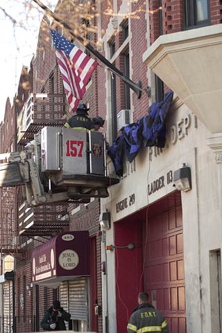 Firefighter Matthew Roberts from Engine 249 and Firefighter Frank Valerio from Ladder 113 hang bunting on the facade of their firehouse in memory of Lt. John Martinson on January 4.