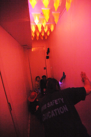 Inside Mobile Fire Safety Experience where children practice fire escape techniques under simulated fire conditions.