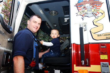Young boy sits in fire truck during outdoor event.