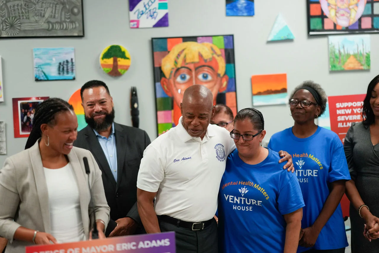 Mayor Adams in white shirt is hugging a person with his left arm