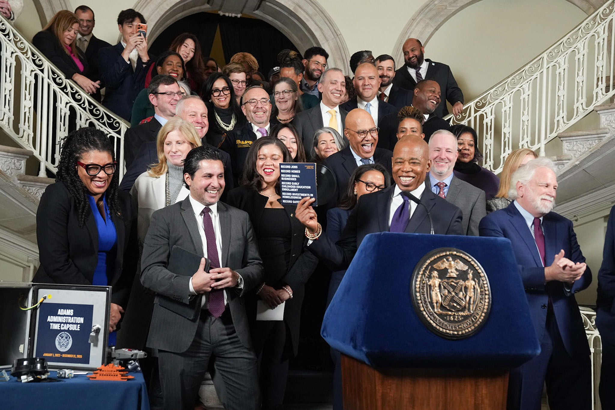 Mayor Adam is seen holding a card, and accompanied by a group of government officials