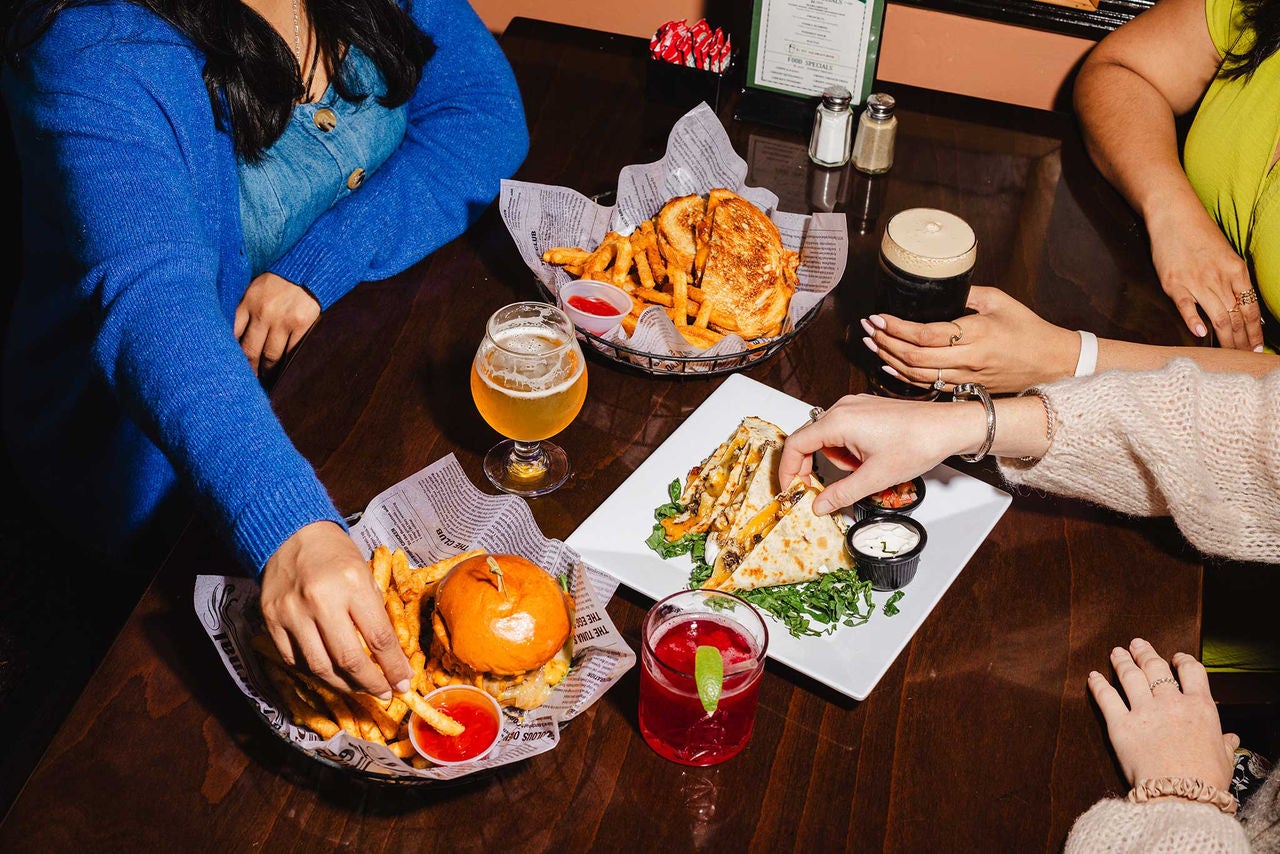 Photo of food on a table with hands reaching for it.