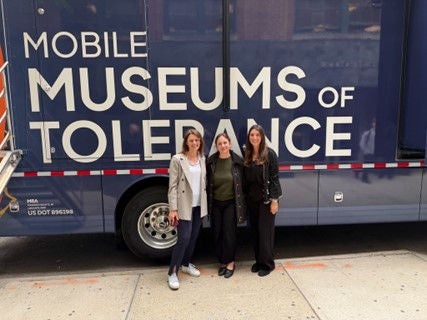 Three women standing in front of a bus with the text Mobile Museum of Tolerance