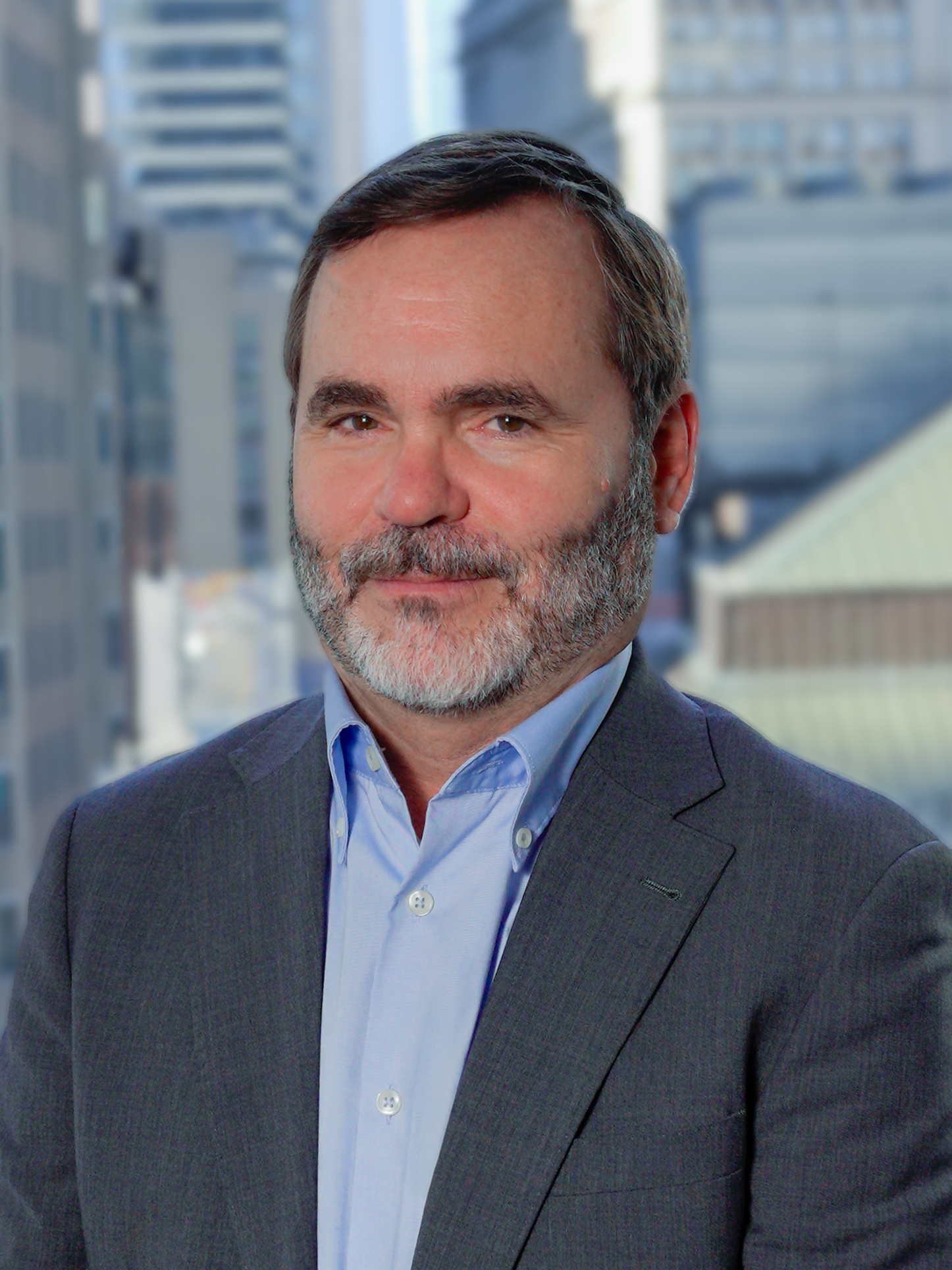 Portrait of Andrew White in a suit, lightly smiling for a photo with a backdrop of city buildings
