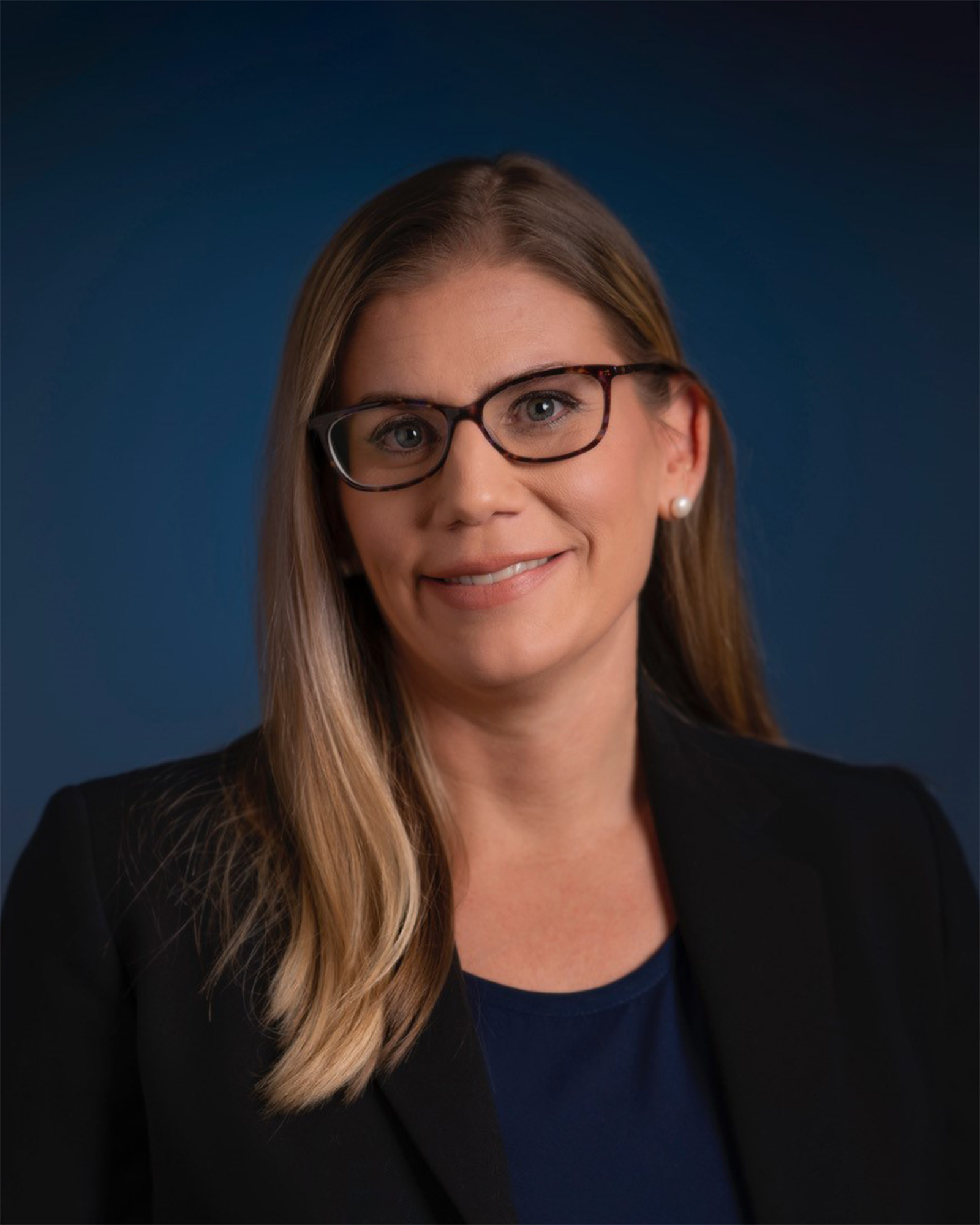 Portrait of Eden Hauslaib in a suit and wearing glasses, smiling for a photo
