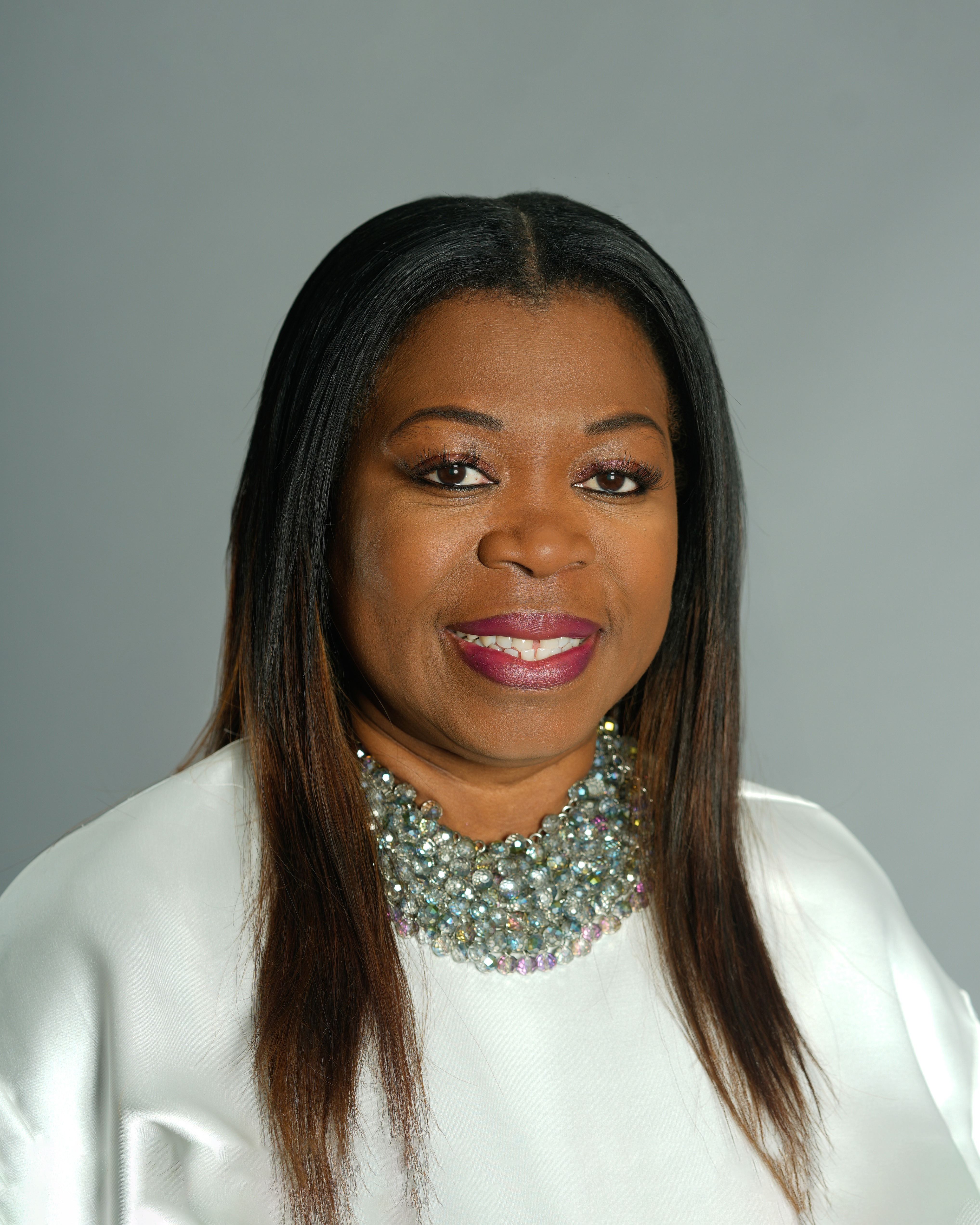 Portrait of Joan Cleary in a white top and many necklaces, smiling for a photo