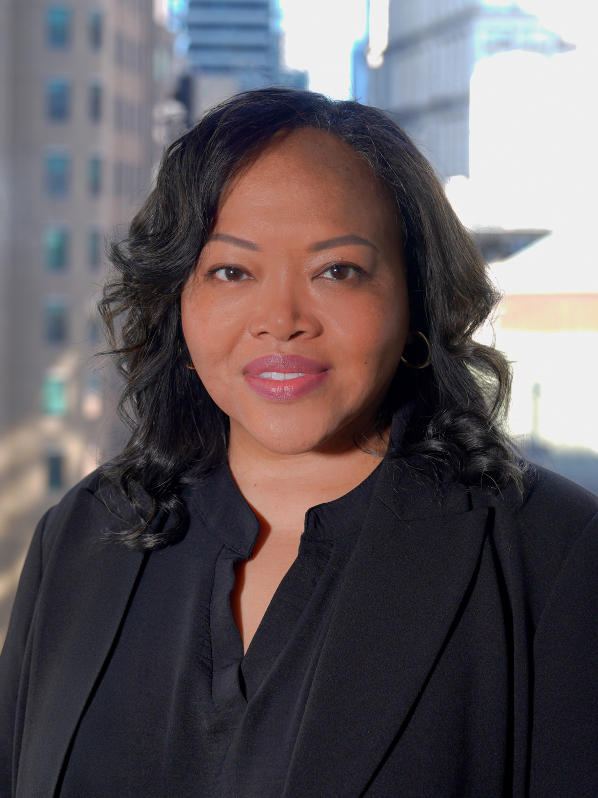 Portrait of Interim Commissioner Melissa Hester in a suit, smiling for a photo with a backdrop of city buildings