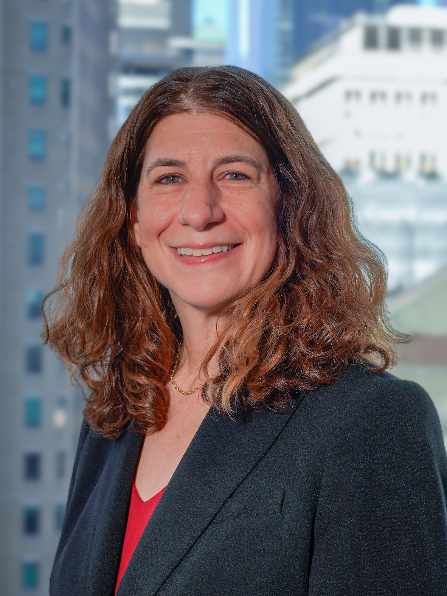 Portrait of Stephanie Gendell in a suit, smiling for a photo with a backdrop of city buildings