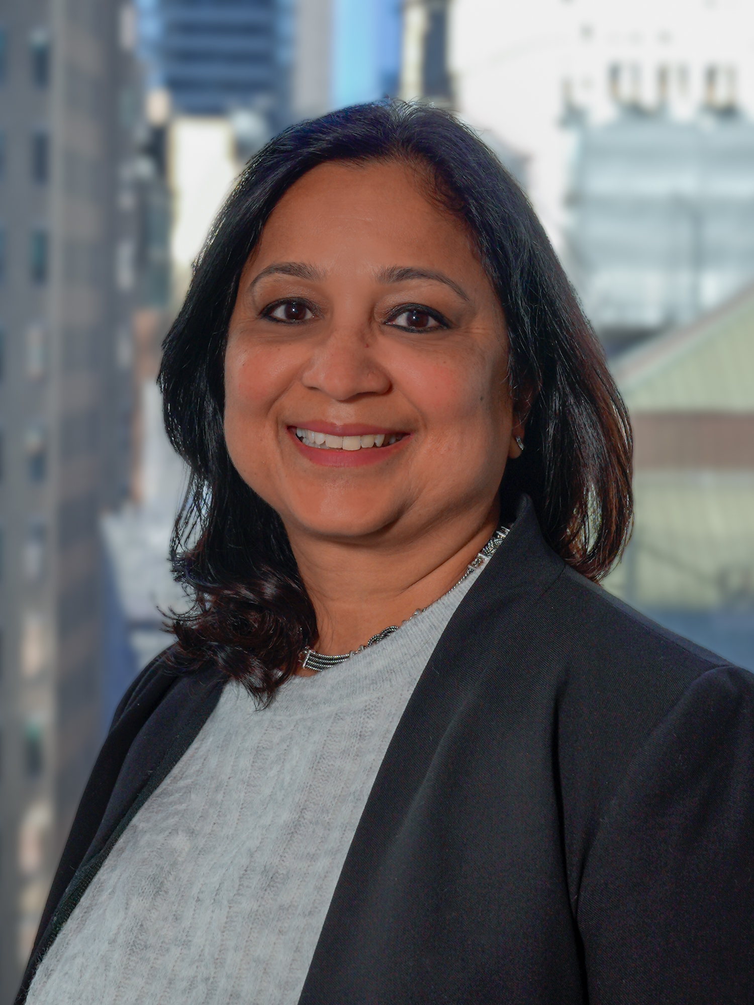 Portrait of Usha Agarwalla in a suit, smiling for a photo with a backdrop of city buildings