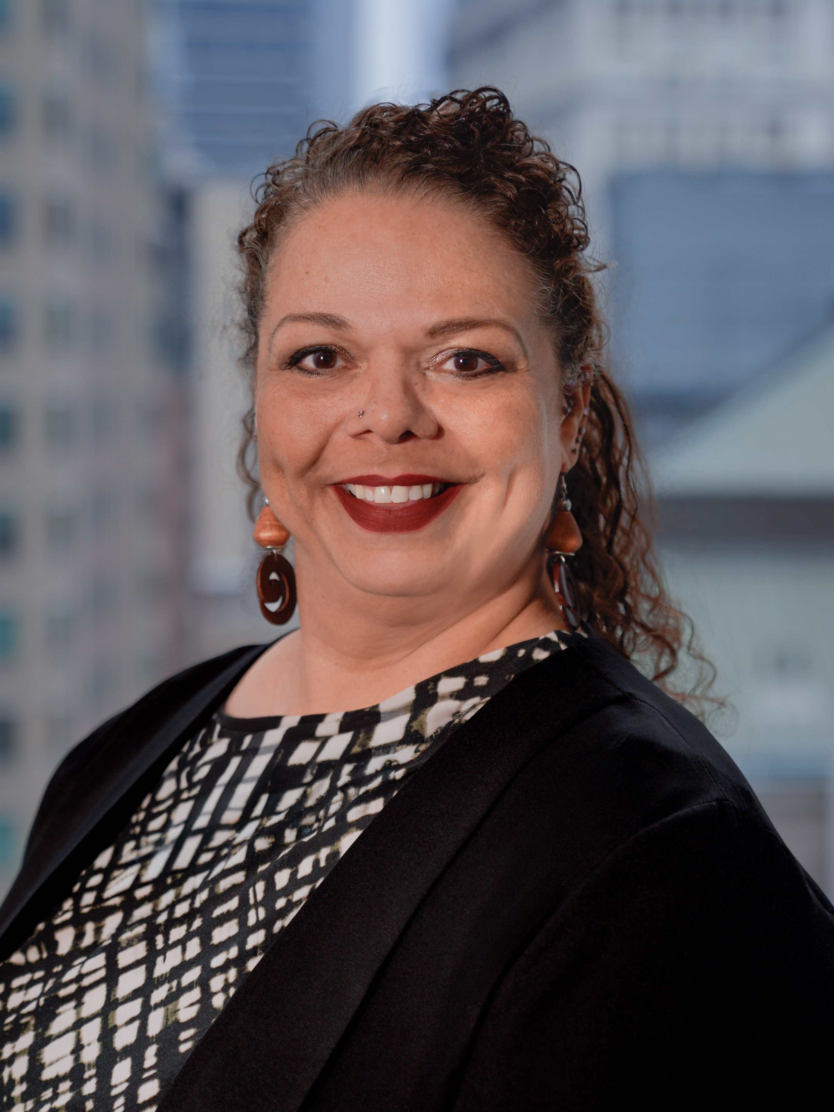 Portrait of Interim Commissioner Melissa Hester in a suit, smiling for a photo with a backdrop of city buildings