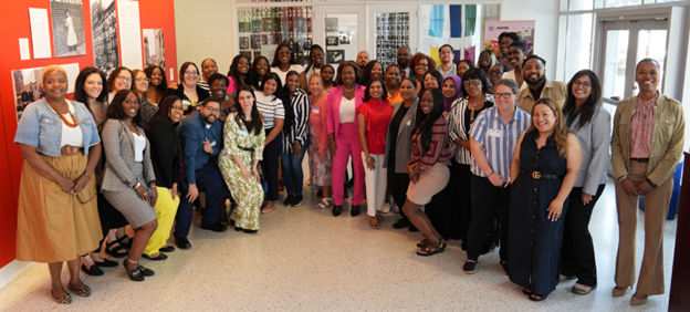 A group of approximately forty people stand side by side next to an orange wall.
