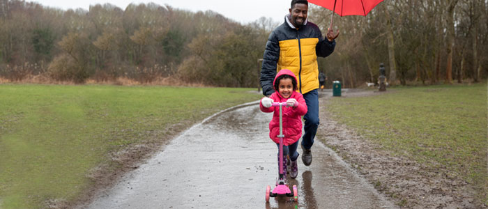 Person holding an umbrella behind a child on a scooter in the rain