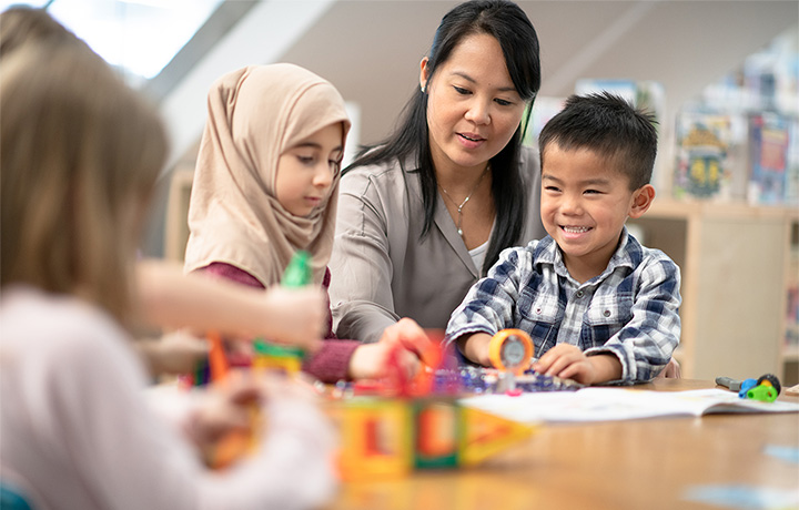 Person playing with three children at table with toys
                                           