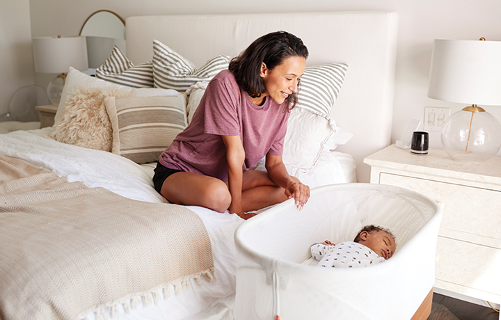 Person sitting on bed alongside a baby in a crib
                                           