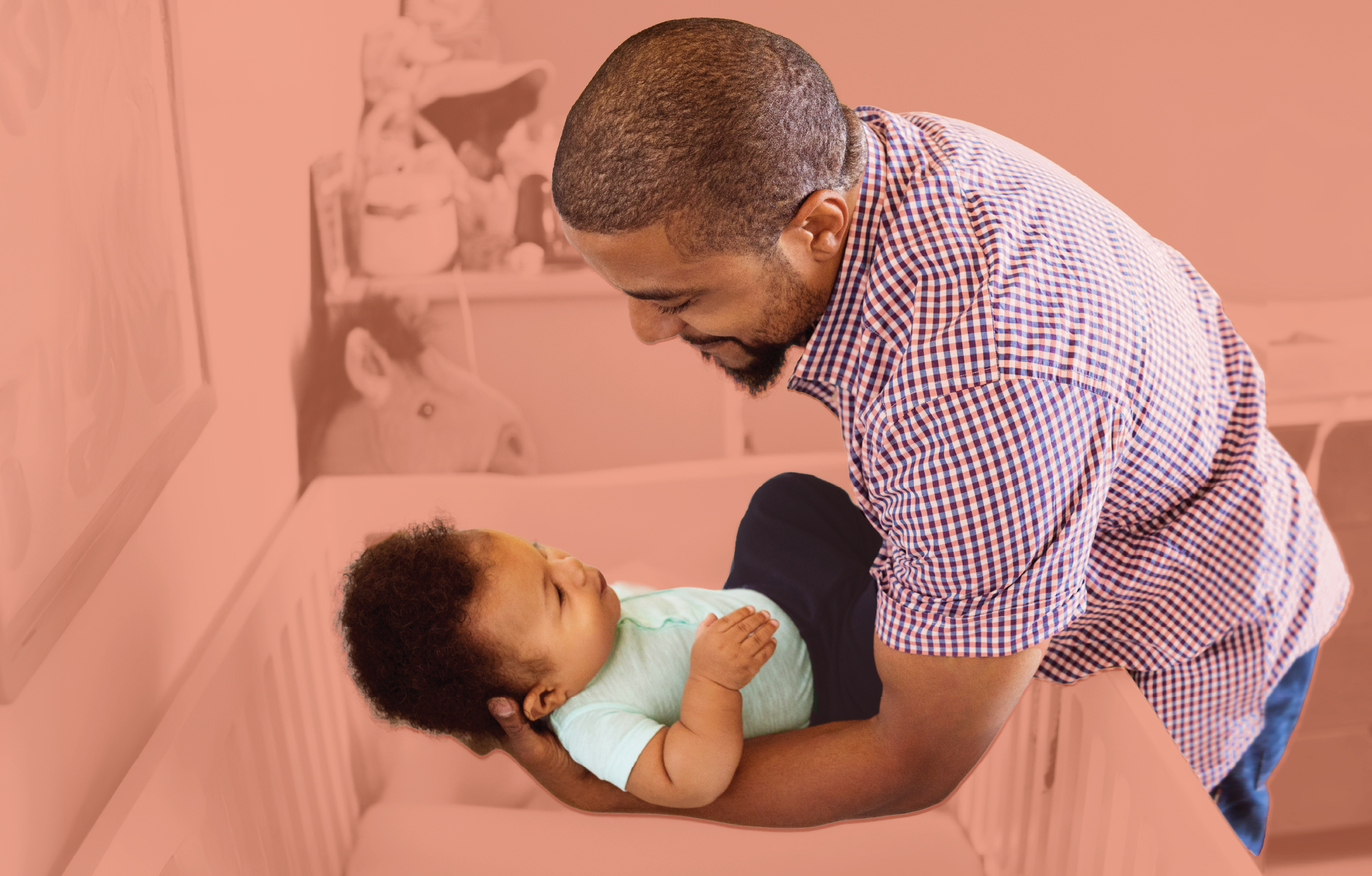 A man is placing a baby into a crib as they look at each other
                                           