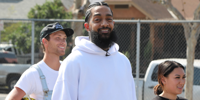 Photo of Nipsey Hussle smiling and wearing a white hoodie as he walks among others