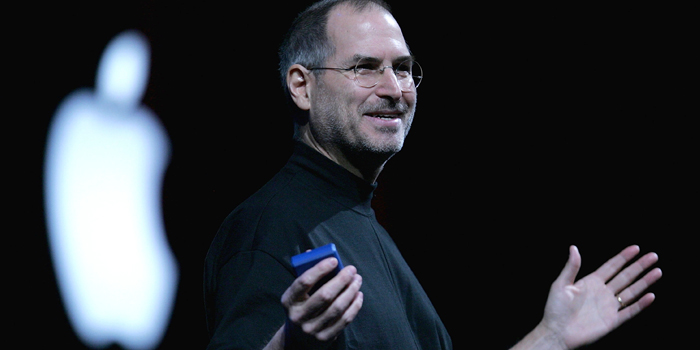 Photo of Steve Jobs with a remote in his hand with a blurred Apple logo in the background