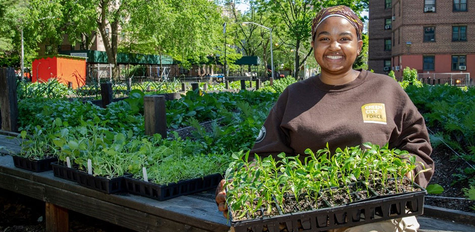Smiling woman holding plants in an outdoor garden in NYC. 
                                           