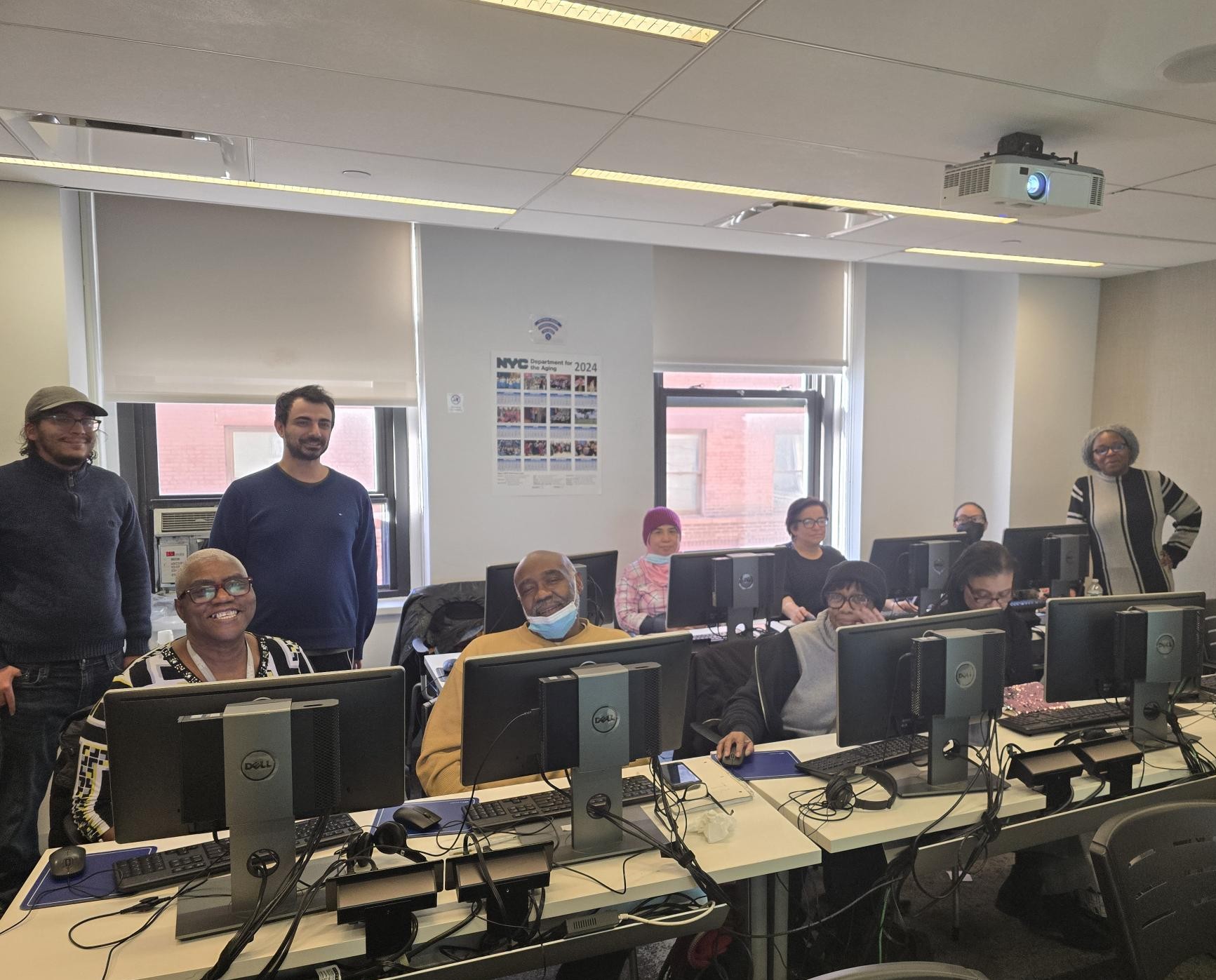 Older adults use desktop computers as trainers assist them during tax training. 