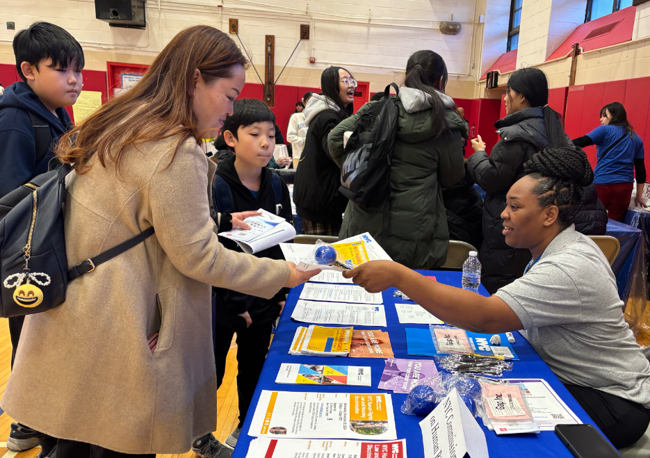 Two people (one Commission staff member and one member of the public) speaking at Commission table, while a seated staff member looks on.