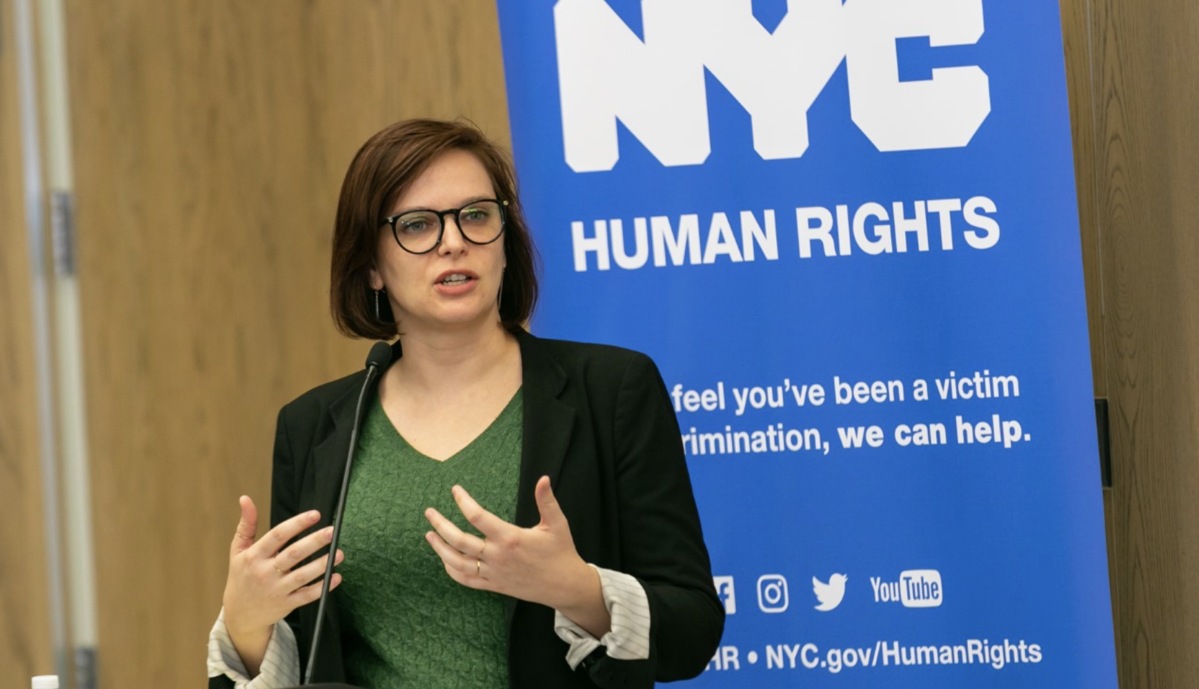Commission staff member speaking at podium with an NYC Human Rights banner behind her.