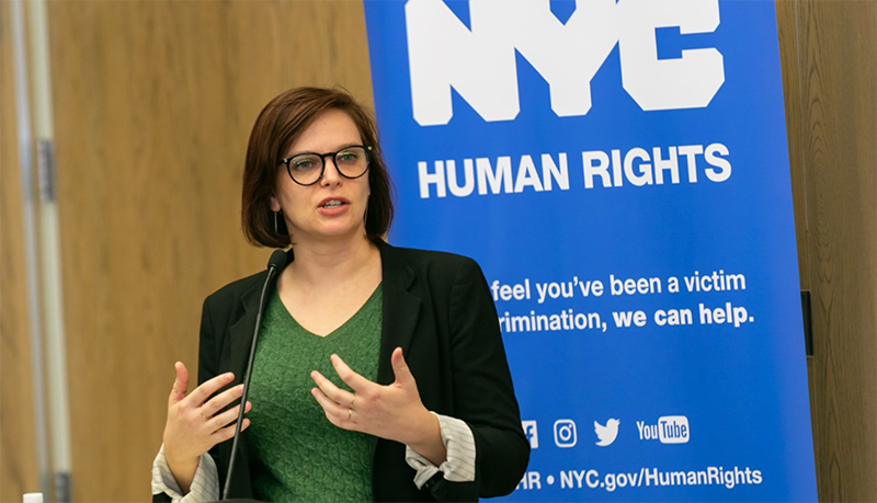 Commission staff member speaking at podium with an NYC Human Rights banner behind her.