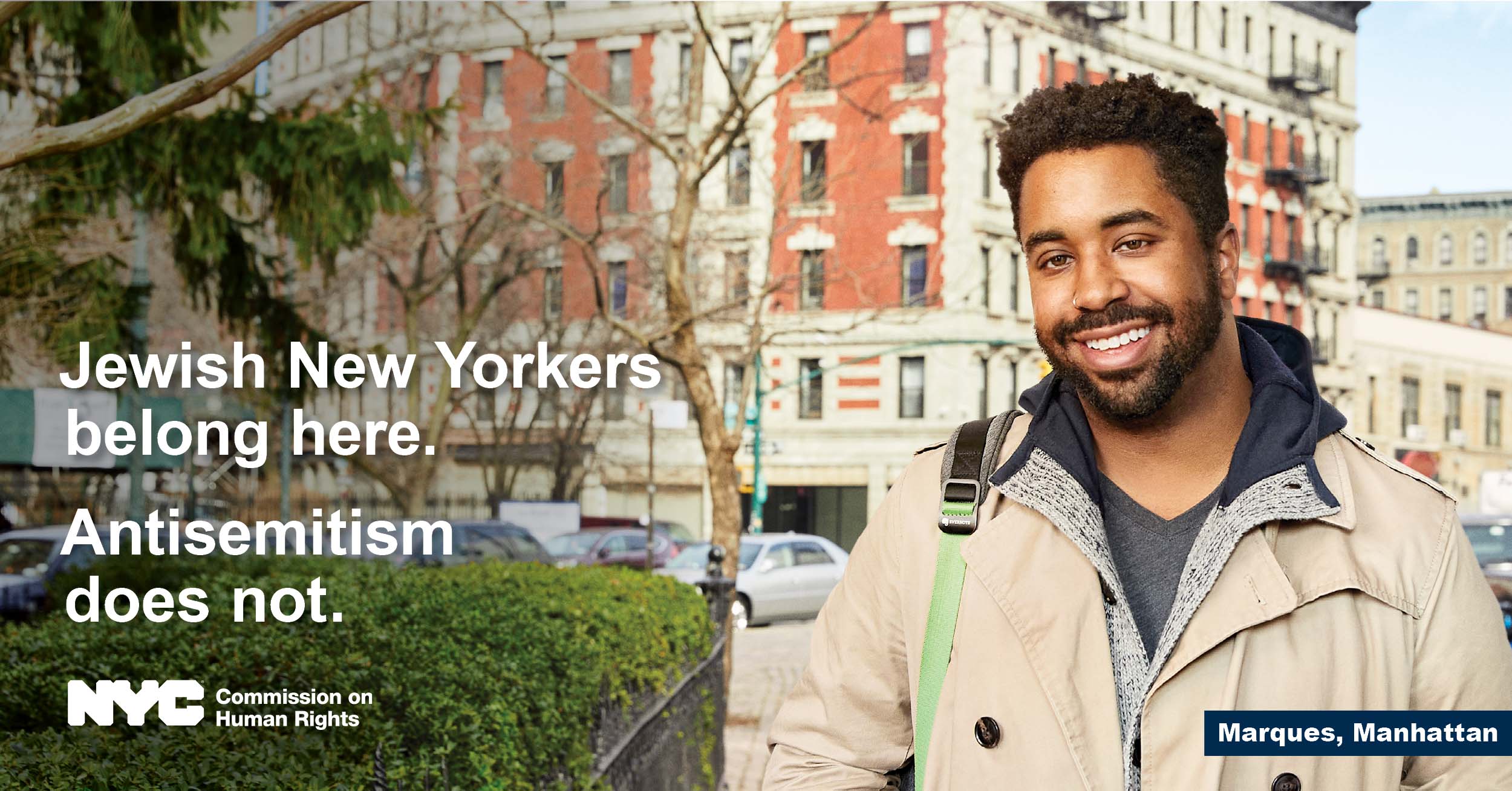 Man in tan jacket looking straight ahead with NYC building in the background.  Text reads, “Jewish New Yorkers belong here. Antisemitism does not.” NYC logo is at the bottom, with NYC Commission on Human Rights.  On the bottom-right, text reads “Marques, Manhattan.” 