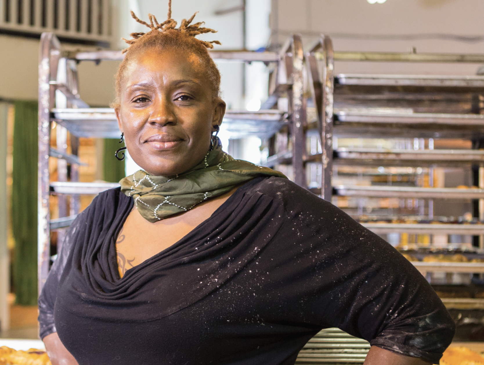 African American  woman looking into camera with a half-smile, with racks of food trays behind her.